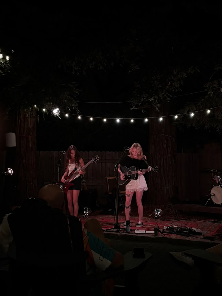 Olivia performing live on an outdoor stage under string lights, with her bassist