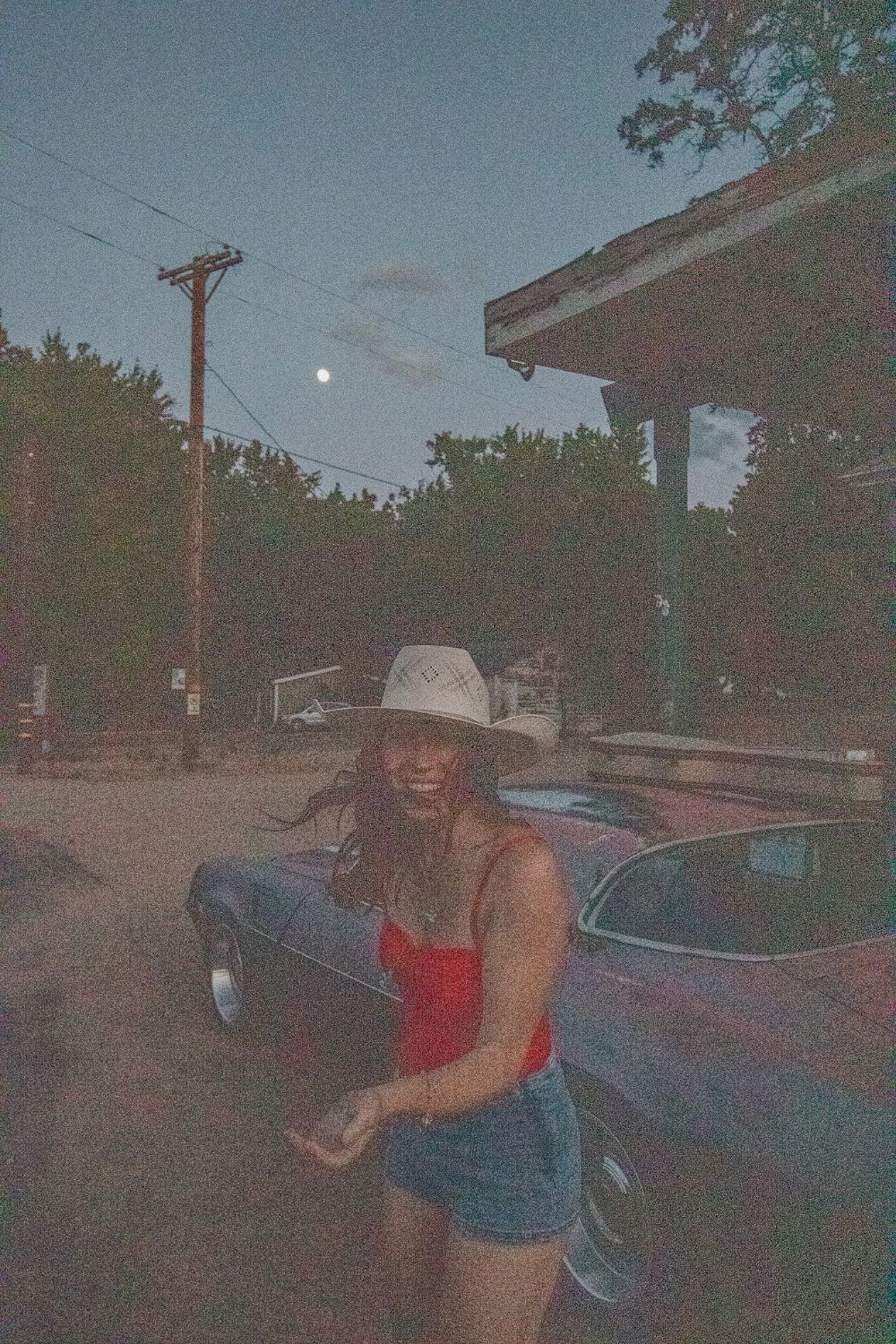 Olivia laughing beside an old car under a rising moon