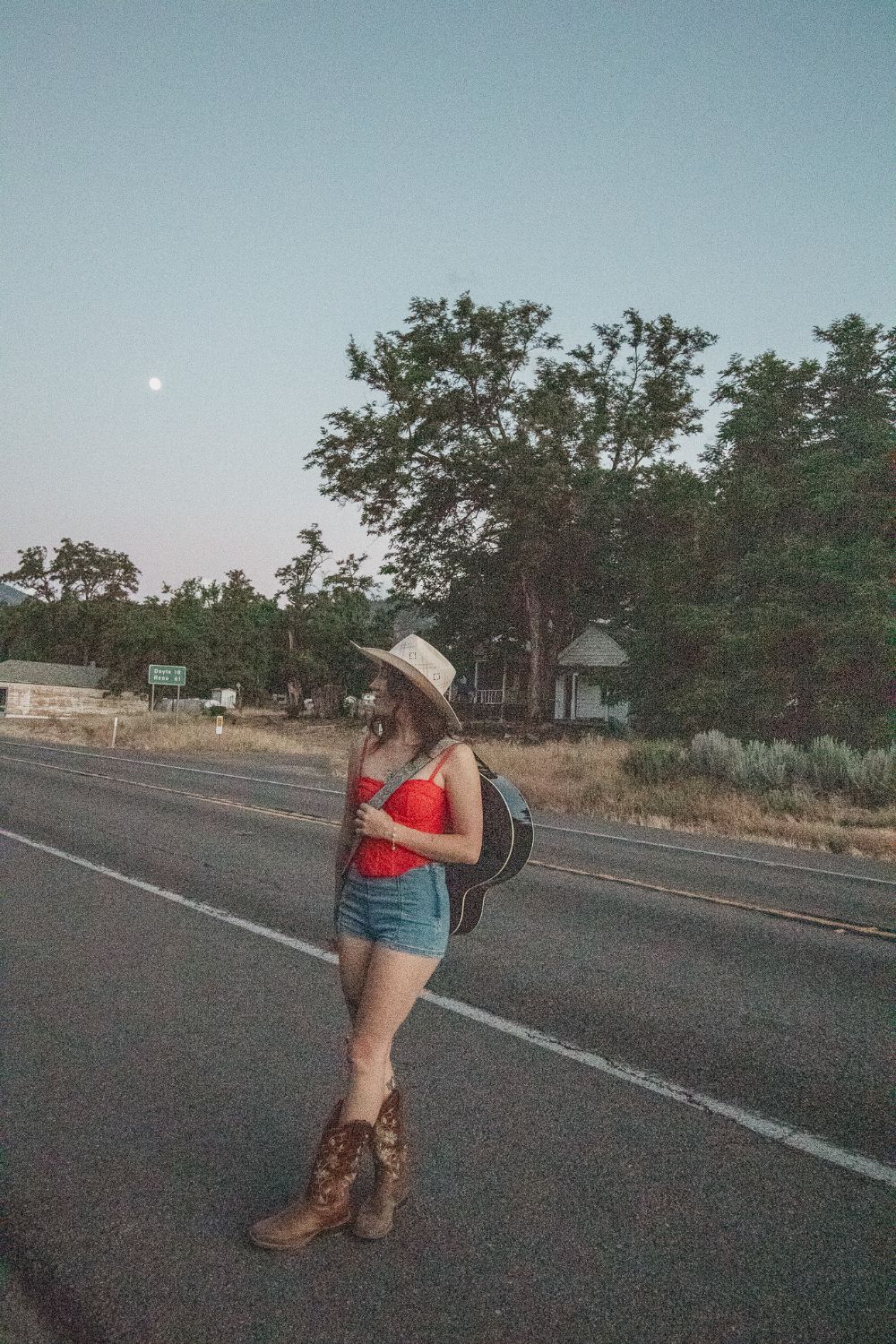 Olivia walking the highway with her guitar slung on her back, moon overhead